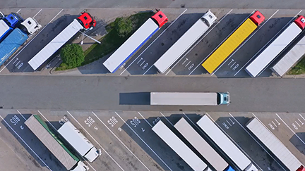 Aerial view of a logistics hub showing semi-trailers parked diagonally in designated truck bays, with one truck driving on the central access road, symbolizing infrastructure efficiency.